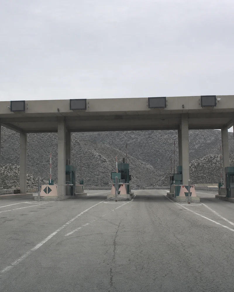 Un poste de péage autoroutier désert, barrières levées et cabines vides, sous un ciel couvert.