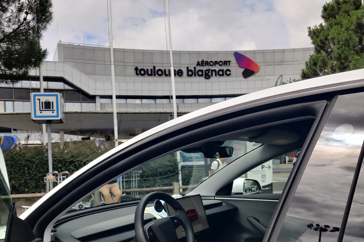 La Tesla Model 3 d’Aude VTC devant l’aérogare de Toulouse-Blagnac, portière passager ouverte.