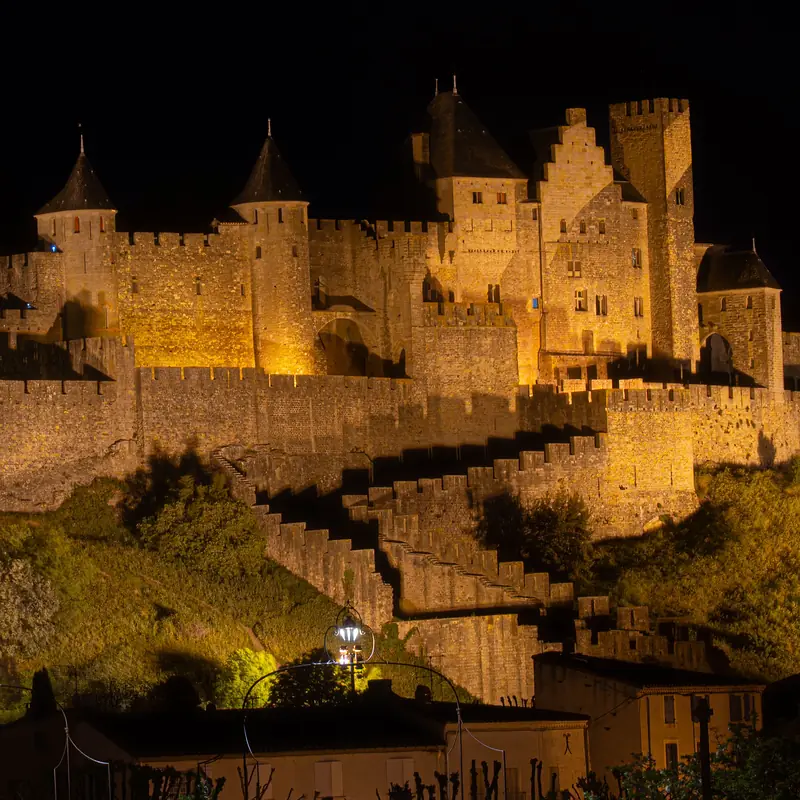 La Cité de Carcassonne illuminée à la nuit tombée : le château comtal et les tours de la double enceinte en lumière dorée sur un ciel noir