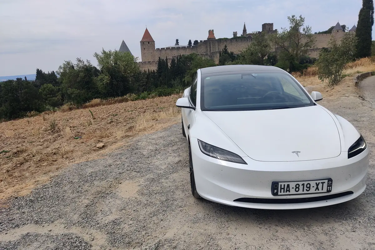 La Tesla Model 3 blanche d’Aude VTC stationnée face aux remparts de la Cité de Carcassonne.