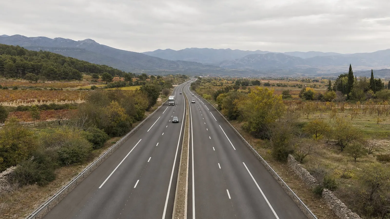 Une autoroute à deux fois deux voies filant vers le sud entre vignes et garrigue, en direction des contreforts des Pyrénées, sur la route de Carcassonne à Barcelone, sous un ciel couvert