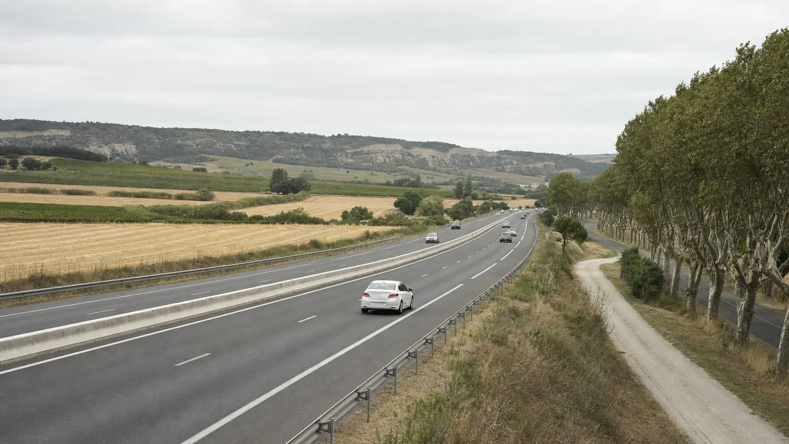 Une autoroute à deux fois deux voies traversant les champs et les collines du Lauragais, entre Carcassonne et Toulouse, sous une lumière couverte