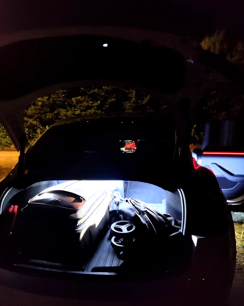 Coffre arrière ouvert et éclairé de la Tesla Model 3, chargé de bagages de voyage.