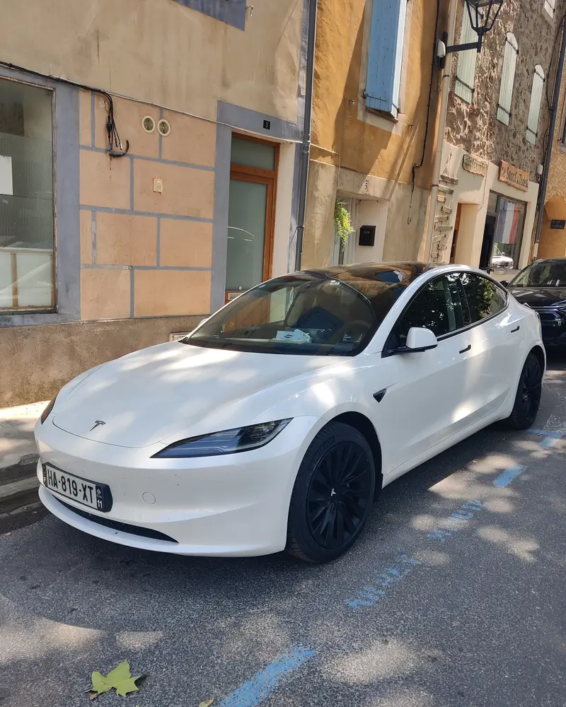 La Tesla Model 3 d’Aude VTC dans une rue de Durban-Corbières, façades ocre et volets bleus.