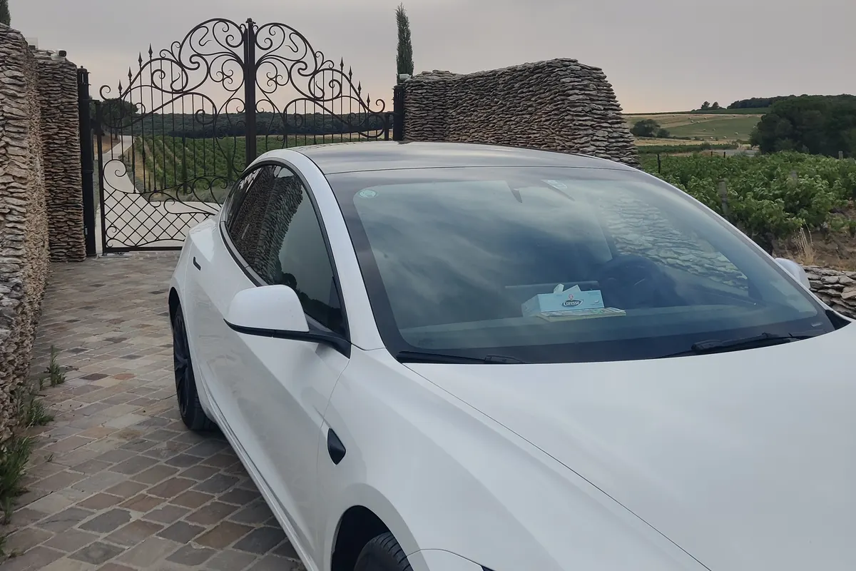 La Tesla Model 3 d’Aude VTC devant la grille d’un domaine viticole du Cabardès, vignes en arrière-plan.